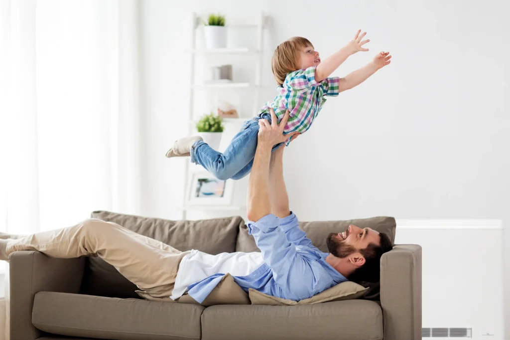Image of father playing with son, with the Elnur ECOHHR PLUS Storage Heater in the background.