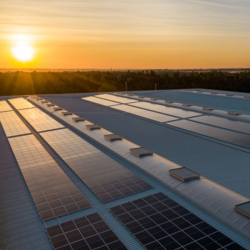 Image of warehouses with solar panels attached to the roof, with the sun setting in the background.