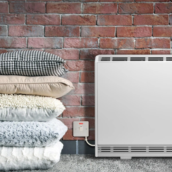 Creda TSRE Fan Assisted Storage Heaters installed in living room, with a brick wall behind it and pillows next to it.