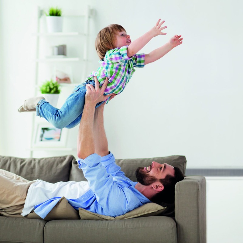Father playing with child, with Elnur ECOSSH Smart Storage Heater in background.